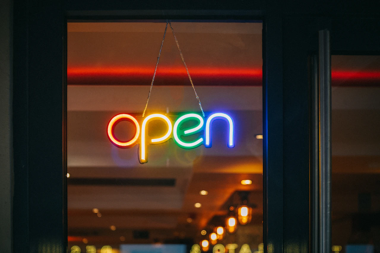 A neon open sign hanging in a shop door, glowing against the warm light inside.