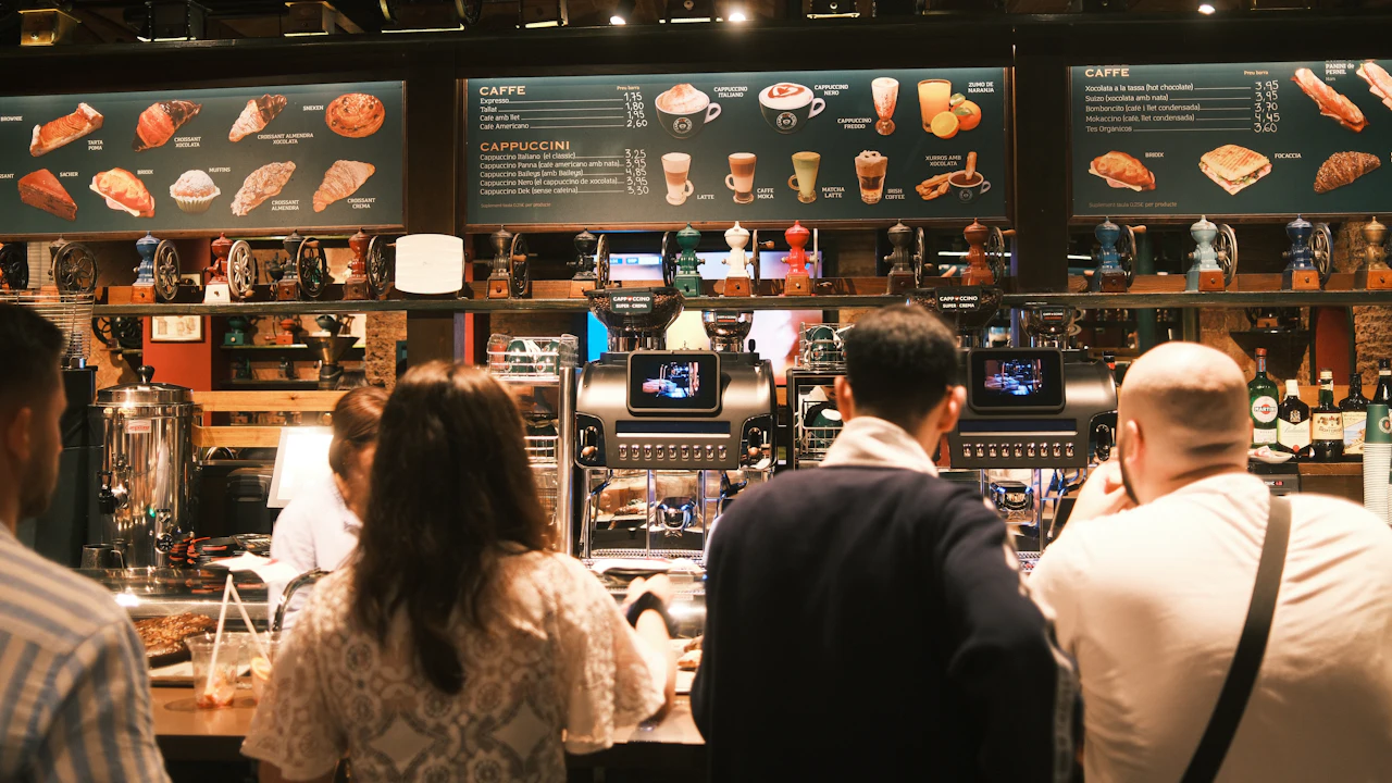 Customers ordering at a café counter under a row of digital menu screens.