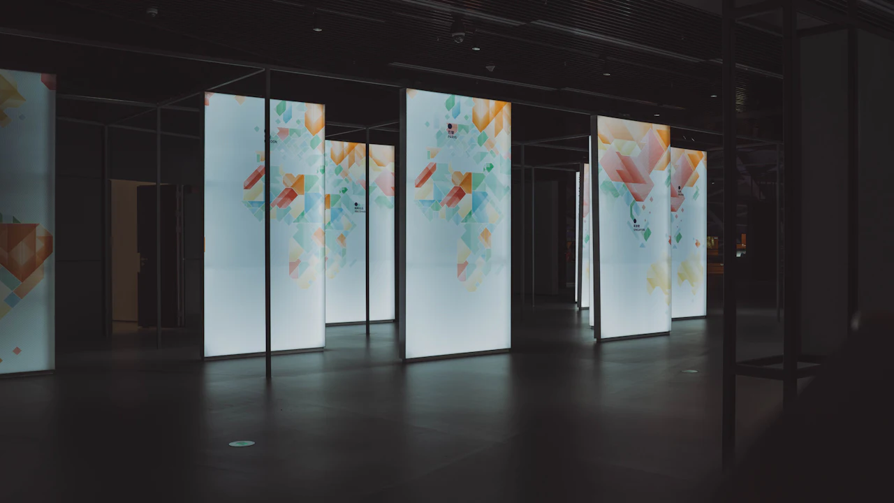 Rows of tall freestanding lit displays showing abstract artwork in a darkened hall.