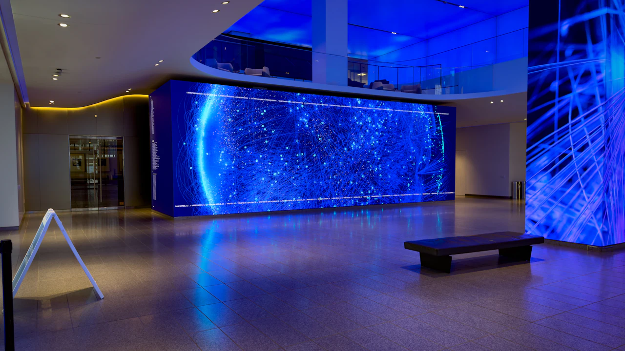 A large LED video wall lit blue across the far side of an empty office lobby.