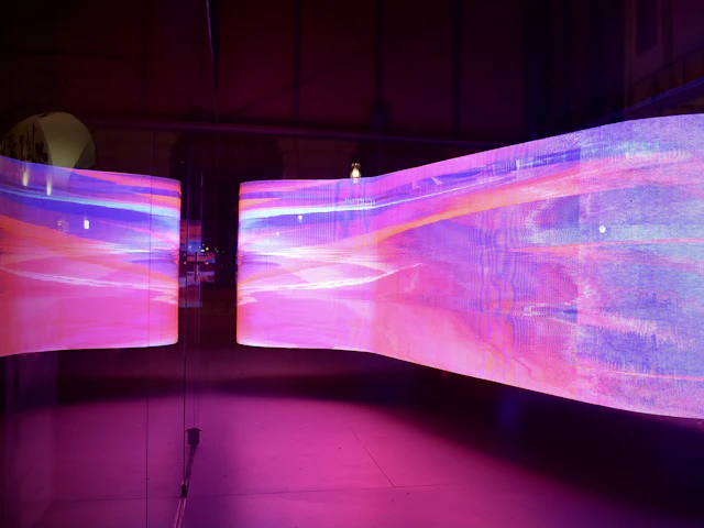 A curved LED display wall glowing with flowing pink and violet light.