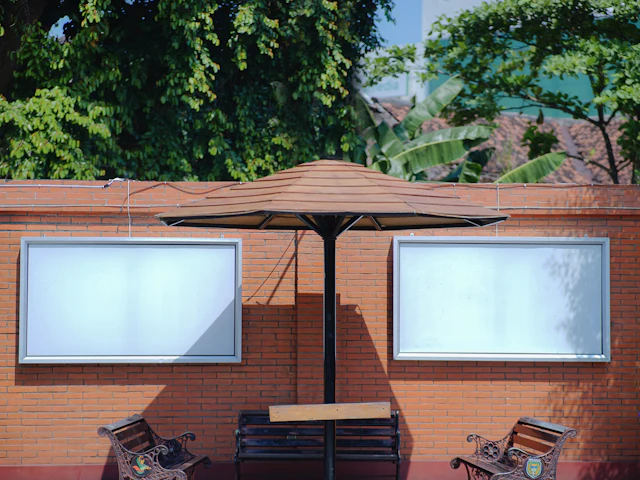 Two outdoor display panels on a brick wall behind café benches and a parasol.