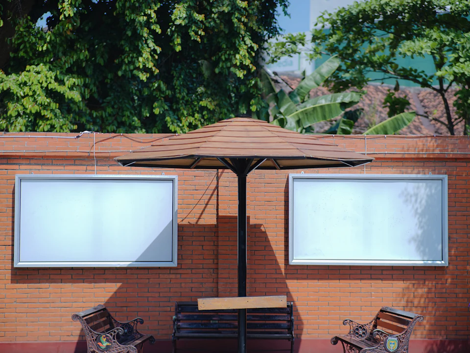 Two outdoor display panels on a brick wall behind café benches and a parasol.