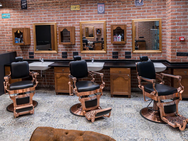 A barber shop interior with a row of chairs against an exposed brick wall.