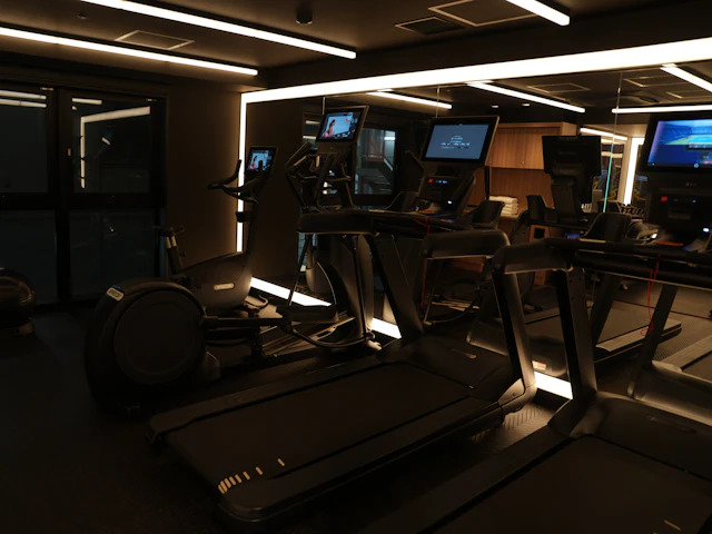A dimly lit gym with a row of treadmills, each with its own screen.